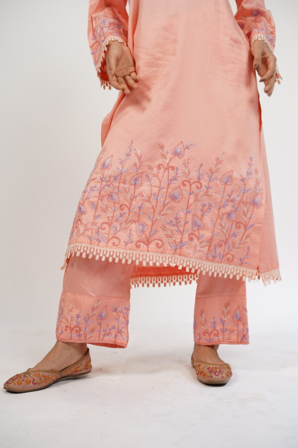 Close-up of Aari embroidery on the hemline of VaadiByLiza’s peach straight kurta set, with intricate floral detailing.