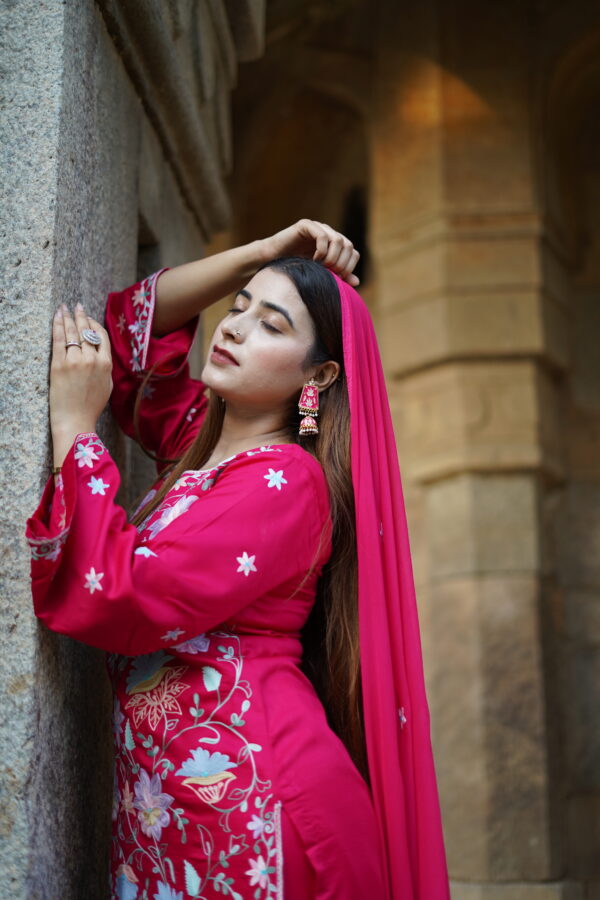 Woman wearing a magenta Aari-embroidered kurta, posing elegantly under an