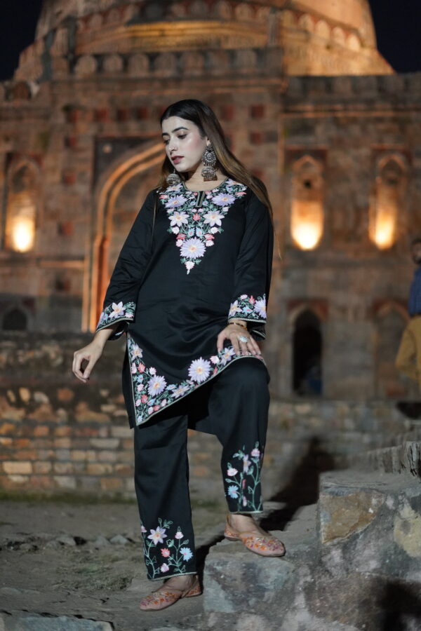 Full view of a black short kurta with floral Aari embroidery, paired with matching pants.